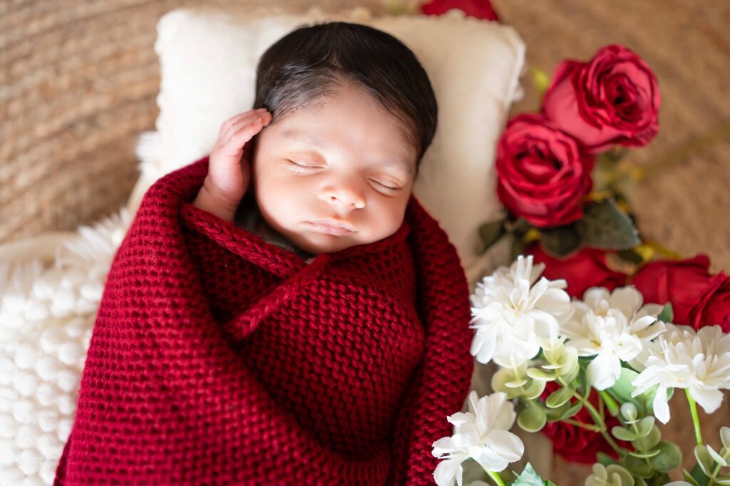 Baby wrapped in beautiful red wrap and setup made with red roses and white flowers, photography done by one of best photographer in Gurgaon